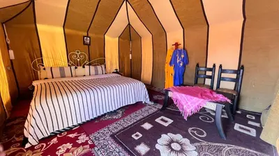 a bedroom with a bed and an umbrella on a rug at Sahara Luxury Camp in Zagora