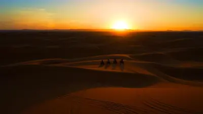 a group of people walking through the desert at sunset at Dunes Luxury Camp in Merzouga