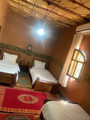 a bedroom with two beds and a window and a rug at Dar nadia bendriss in Ouarzazate