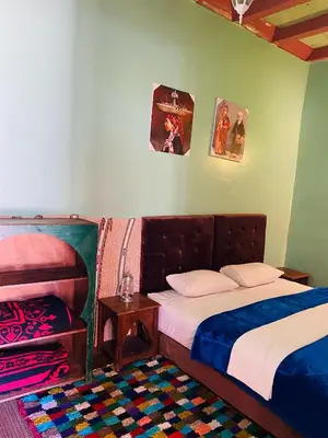 a bedroom with two beds and a table and pictures on the wall at Kasbah Ait Bouguemez in Agouti