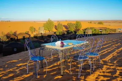 a table and chairs in the middle of the desert at Mustapha Camp Merzouga in Merzouga