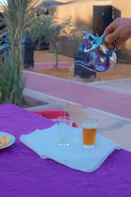 a person pouring a drink into a glass on a table at Mustapha Camp Merzouga in Merzouga