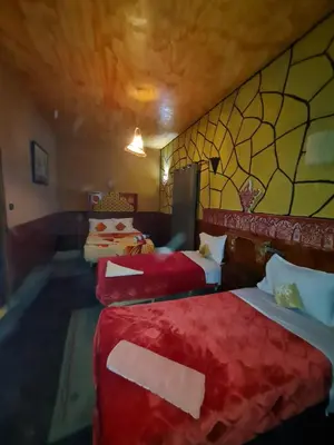 a hotel room with three beds with red sheets at Riad Tigmi du Soleil in Aït Ben Haddou