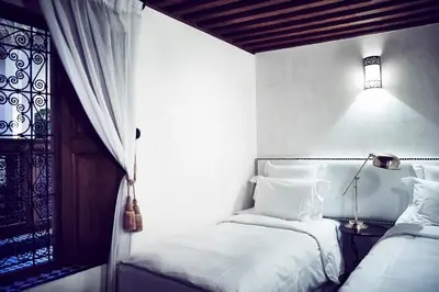a white bedroom with two beds and a lamp at Chaq Chaq in Fès