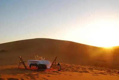 a man standing in front of a table in a desert at Boho Glamping in Merzouga