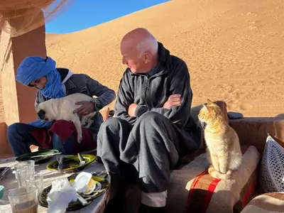 two people and a cat sitting on a couch in the desert at Dar Nomads in Mhamid