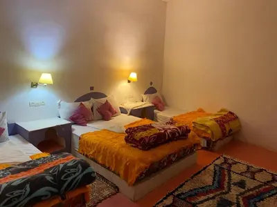 a room with three beds with orange sheets at Hôtel familiale les grotte in Aït Ben Haddou