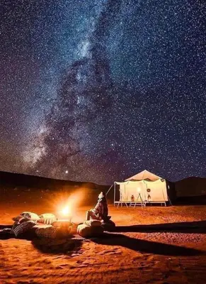 a man sitting in front of a tent under the stars at Mhamid Tours in Mhamid
