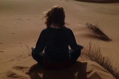 a person is sitting in a meditation pose in the desert at Mhamid Tours in Mhamid
