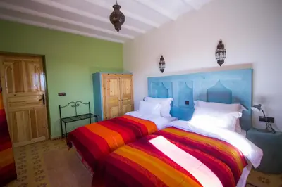 a bedroom with two beds with colorful striped sheets at Hassilabiad Appart Hotel in Merzouga