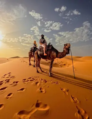 two people riding on a camel in the desert at Erg Chigaga Camp Shooting Stars in Mhamid
