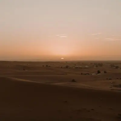 a sunset in the desert with the sun setting in the horizon at Erg Chigaga Camp Shooting Stars in Mhamid