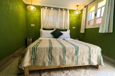 a bedroom with a bed with green walls and windows at Dar Soufian in Ouarzazate