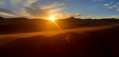 a sunset in the desert with the sun setting at Erg Merzouga Desert Camp in Merzouga