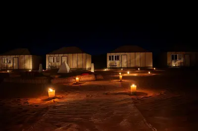 a group of huts at night with candles in the sand at Bivouac Luna in Mhamid