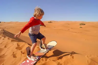 a young boy standing on a surfboard in the desert at Merzouga Berbers Luxury Camp in Merzouga