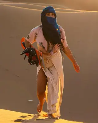 a woman walking on the beach with a snowboard at Merzouga Berbers Luxury Camp in Merzouga