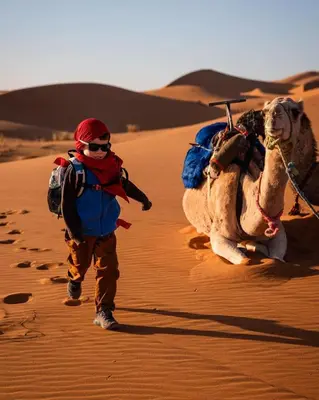 a boy walking with a camel in the desert at Merzouga Berbers Luxury Camp in Merzouga