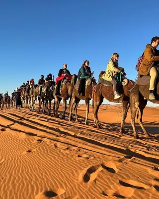 a group of people riding on camels in the desert at Merzouga Berbers Luxury Camp in Merzouga
