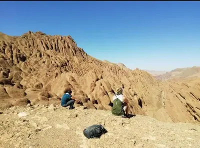 two people sitting on a rock formation in the desert at Auberge Restaurant Zahra in Boumalne