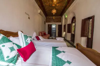 a bedroom with two beds with white sheets and red pillows at Dar Lalla Kenza in Fès