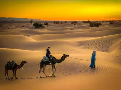 two people riding camels in the desert at sunset at Authentique berber Camp & Activities in Mhamid