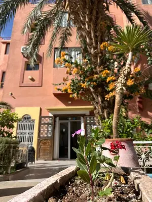 a building with a palm tree and flowers in a garden at Hotel Riad Amlal in Ouarzazate
