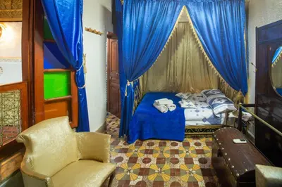 a bedroom with a bed with blue curtains and a chair at Dar Lalla Bouchra in Fès