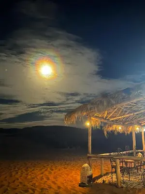 a table with a straw umbrella on the beach at night at Sahara Bedouins Camp in Hassilabied