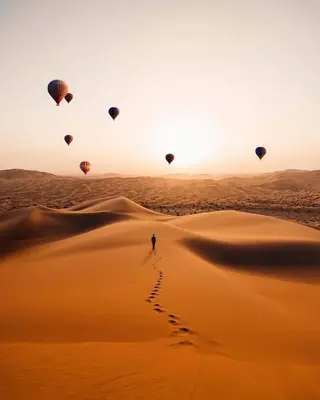 a person is standing in the desert with hot air balloons at Camel Trekking Desert Camp in Merzouga