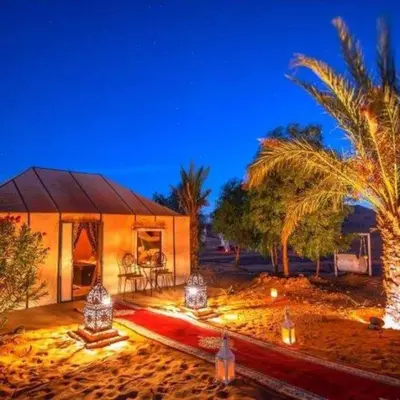 a home in the desert with palm trees and lights at Camel Trekking Desert Camp in Merzouga