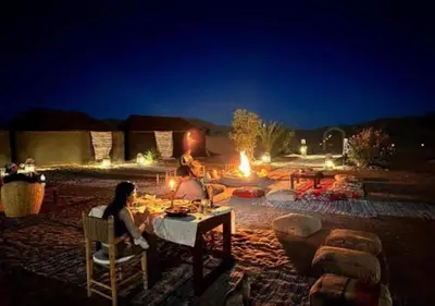 two people sitting at a table in front of a fire pit at Camel Trekking Desert Camp in Merzouga
