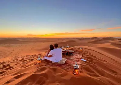 a couple sitting at a table in the desert at Camel Trekking Desert Camp in Merzouga