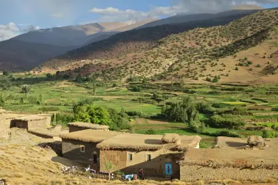 a group of houses in a field with mountains in the background at Dar Ait Bouguemez in Azilal