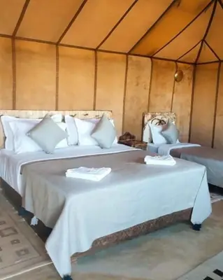 two beds in a tent with white sheets at Blue Sky Luxury Camp in Merzouga