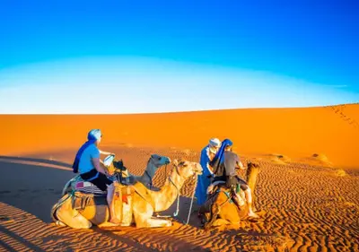 three people riding on camels in the desert at glamping Dunes CAMP in Merzouga