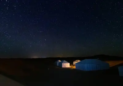 a group of three white tents under a starry sky at glamping Dunes CAMP in Merzouga