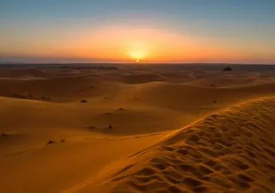 a sunset in the desert with a road in the sand at glamping Dunes CAMP in Merzouga