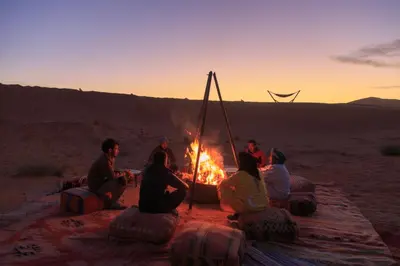 a group of people sitting around a fire in the desert at Tiziri Camp in Merzouga