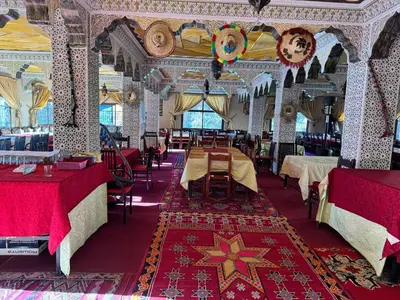 a dining room with tables and chairs and a red rug at AUBERGE ROYAL PALMAS in Tinerhir