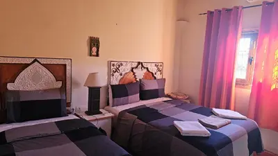 a bedroom with two beds and a window with pink curtains at Tizi Maison d'Hôtes in Telouet