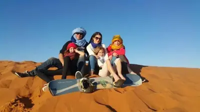 a group of people sitting on the sand with a snowboard at Sahara Nomad Camp in Merzouga