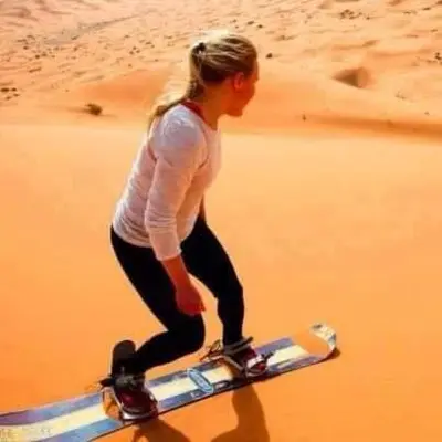 a woman walking on a surfboard on the beach at Sahara Nomad Camp in Merzouga