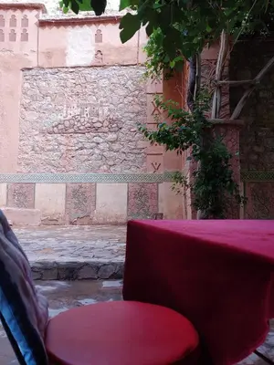 a red table with a red chair in front of a stone wall at Riad Atlas Berbère in Boumalne