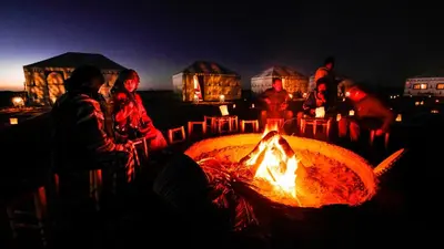 a group of people sitting around a fire pit at night at Sahara Magic Camp in Merzouga
