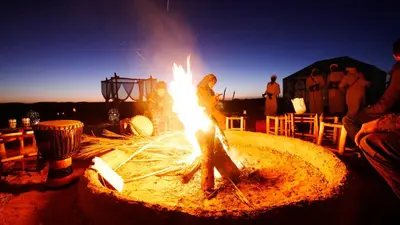 a group of people standing around a fire pit at Sahara Magic Camp in Merzouga