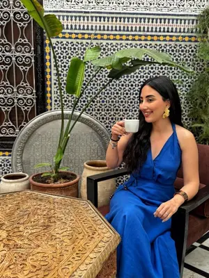 a woman in a blue dress holding a cup of coffee at Riad Tizwa Fes in Fès