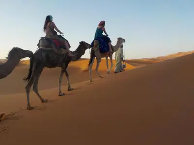 two women riding on camels in the desert at Camel Trek Bivouac in Merzouga