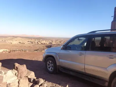 a suv parked in the desert with a herd of animals at Camel Trek Bivouac in Merzouga