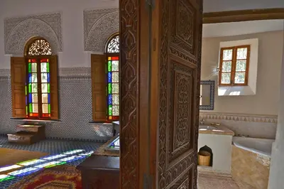 a bathroom with a wooden door with a tub and stained glass at Dar Roumana in Fès